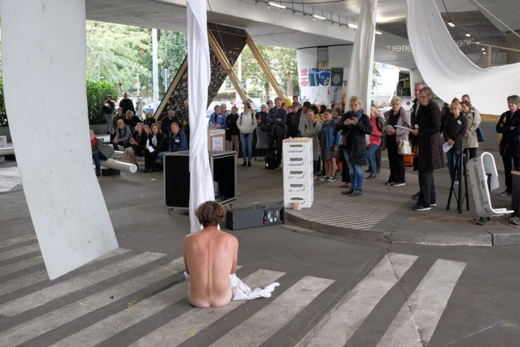 Bild: Künstler sitzt nackt und in Segeltuch gewickelt auf dem Boden