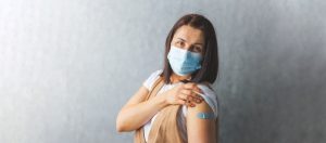 Bild: geimpfe Frau mit Pflaster am Arm und Maske lächelt