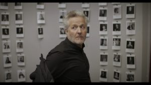 Bild: Mann blickt sich um, im Hintergrund Fotos.