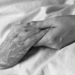Eine Hand hält eine andere ältere Hand auf einem Laken, in schwarz weiß