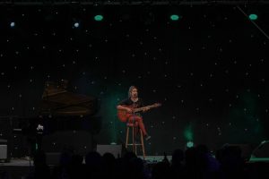 Bild: Musikerin mit Gitarre auf Hocker beim Singen
