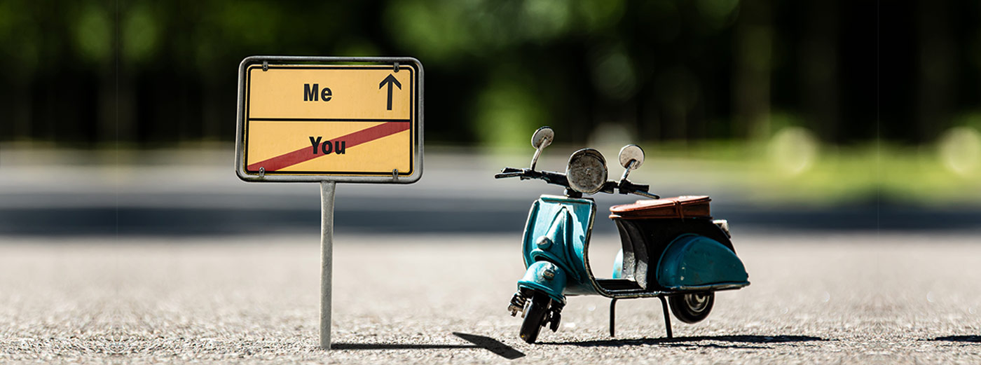 Slider: BIld kleine Vespa steht neben Straßenschild, in die eine Richtung geht es nach Me, in die andere nach You