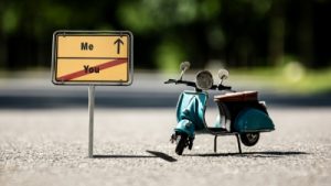 BIld: kleine Vespa steht neben Straßenschild. In die eine Richtung geht es nach Me, in die andere nach You.