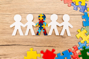 Bild: ausgeschnittene Figuren in Strichmännchen-Form in weiß halten sich an den Händen und in der Mitte ist eines, dass aus bunten Puzzleteilen besteht.